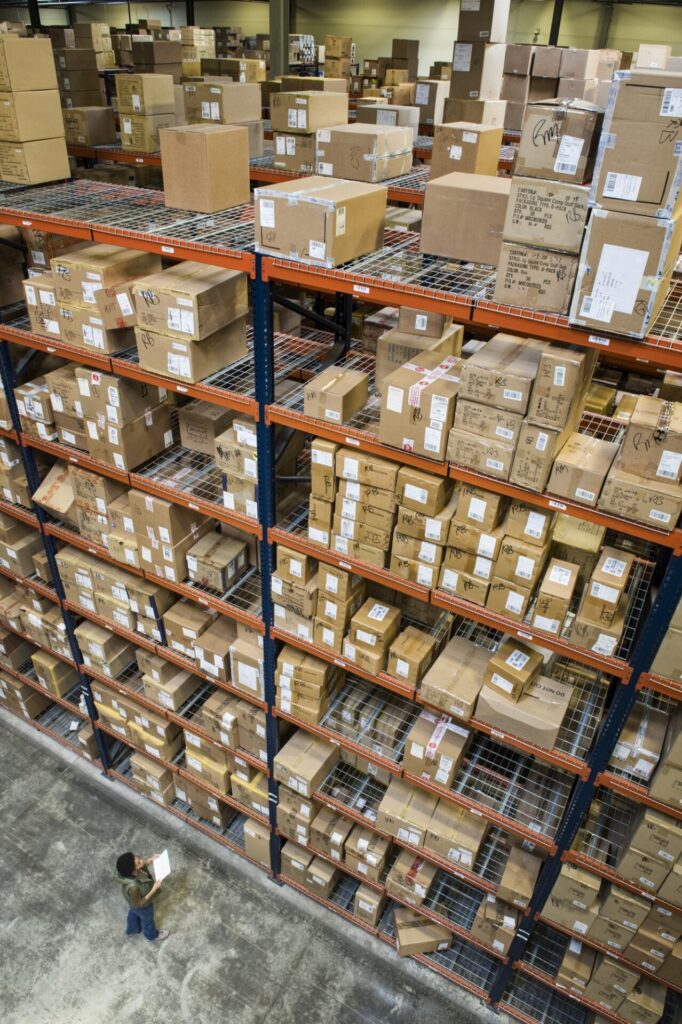 Warehouse worker checking inventory of boxes on racks in a distribution warehouse.