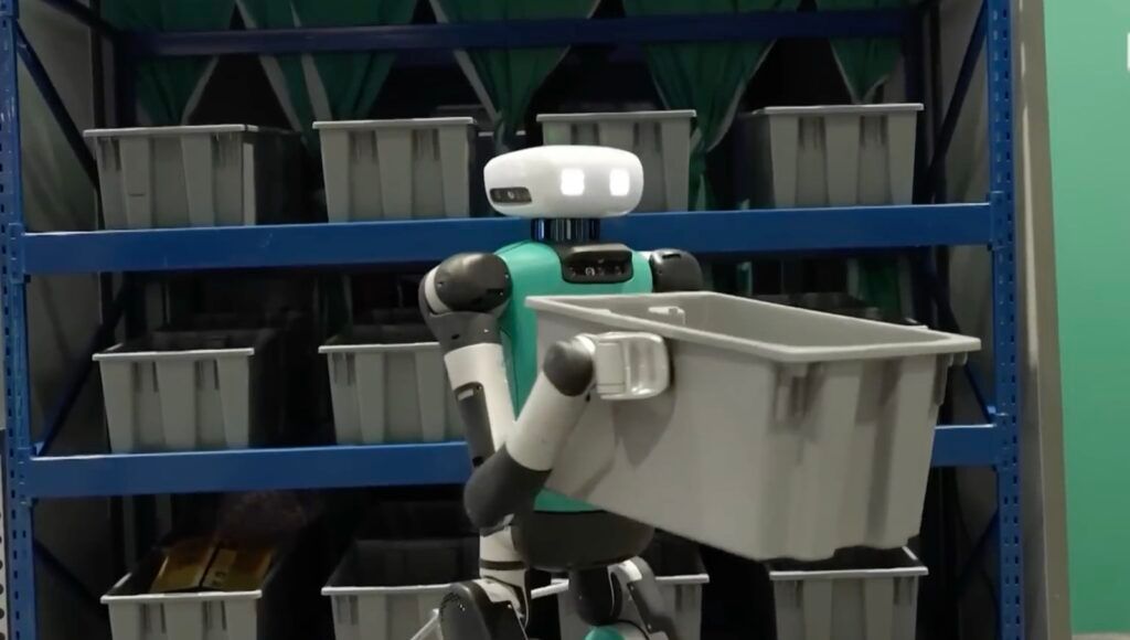 Digit, the bipedal humanoid robot by Agility Robotics, carrying an empty tote in a warehouse test area