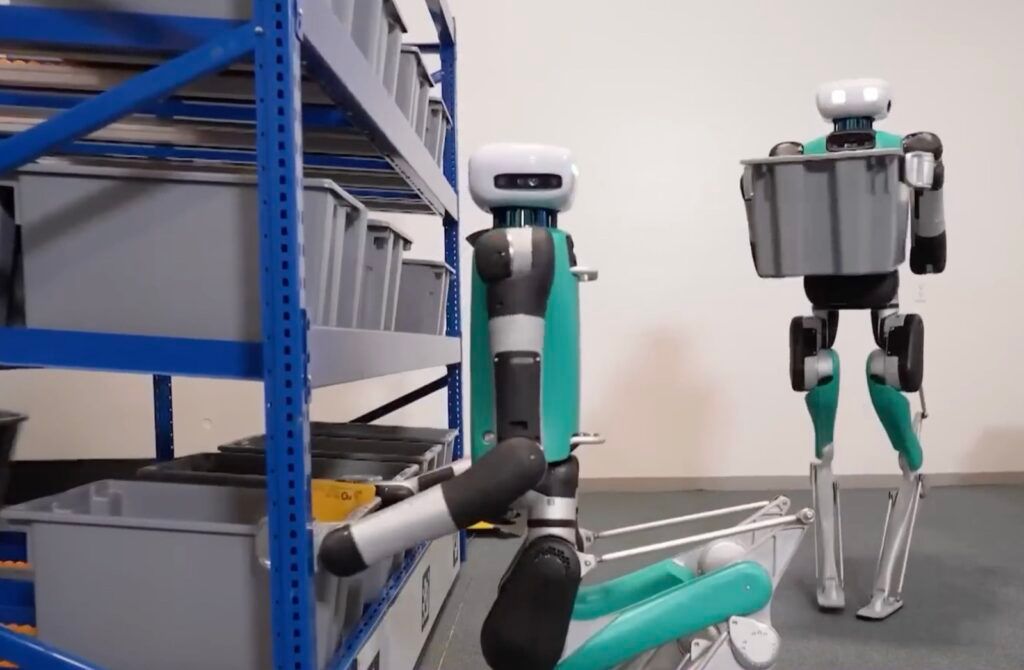 Two Digit bipedal robots moving totes between shelves during tote recycling tests