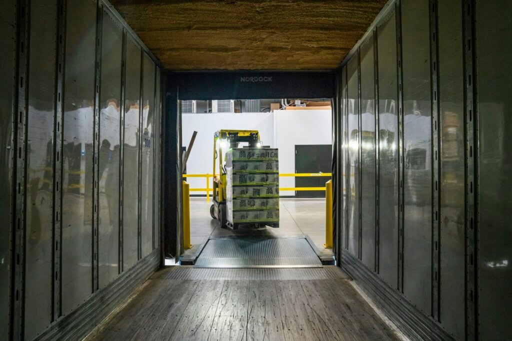 Forklift loading a pallet of goods into a truck trailer, seen from inside the trailer