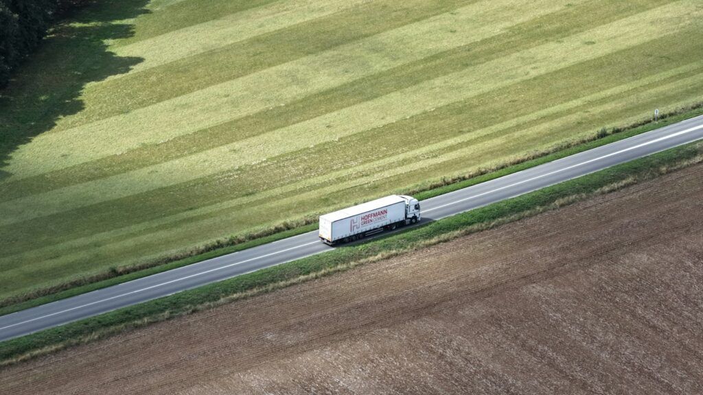 Aerial view of a white truck driving on a road through green fields