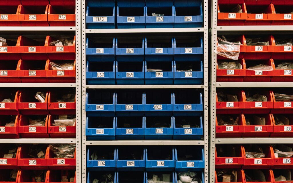 Rows of red and blue open-front plastic bins on warehouse shelving
